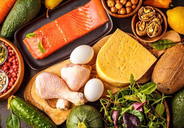 Healthy ingredients for a keto diet, including avocados, eggs, nuts, leafy greens, and salmon, arranged on a wooden table, highlighting the low-carb, high-fat foods that support weight loss and metabolic health.